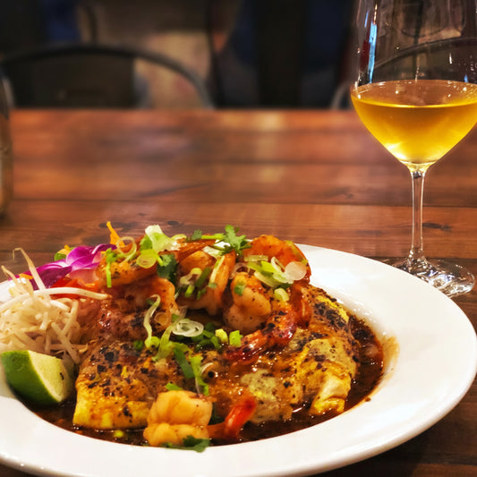 A glass of white wine and a Thai dish on a wooden table